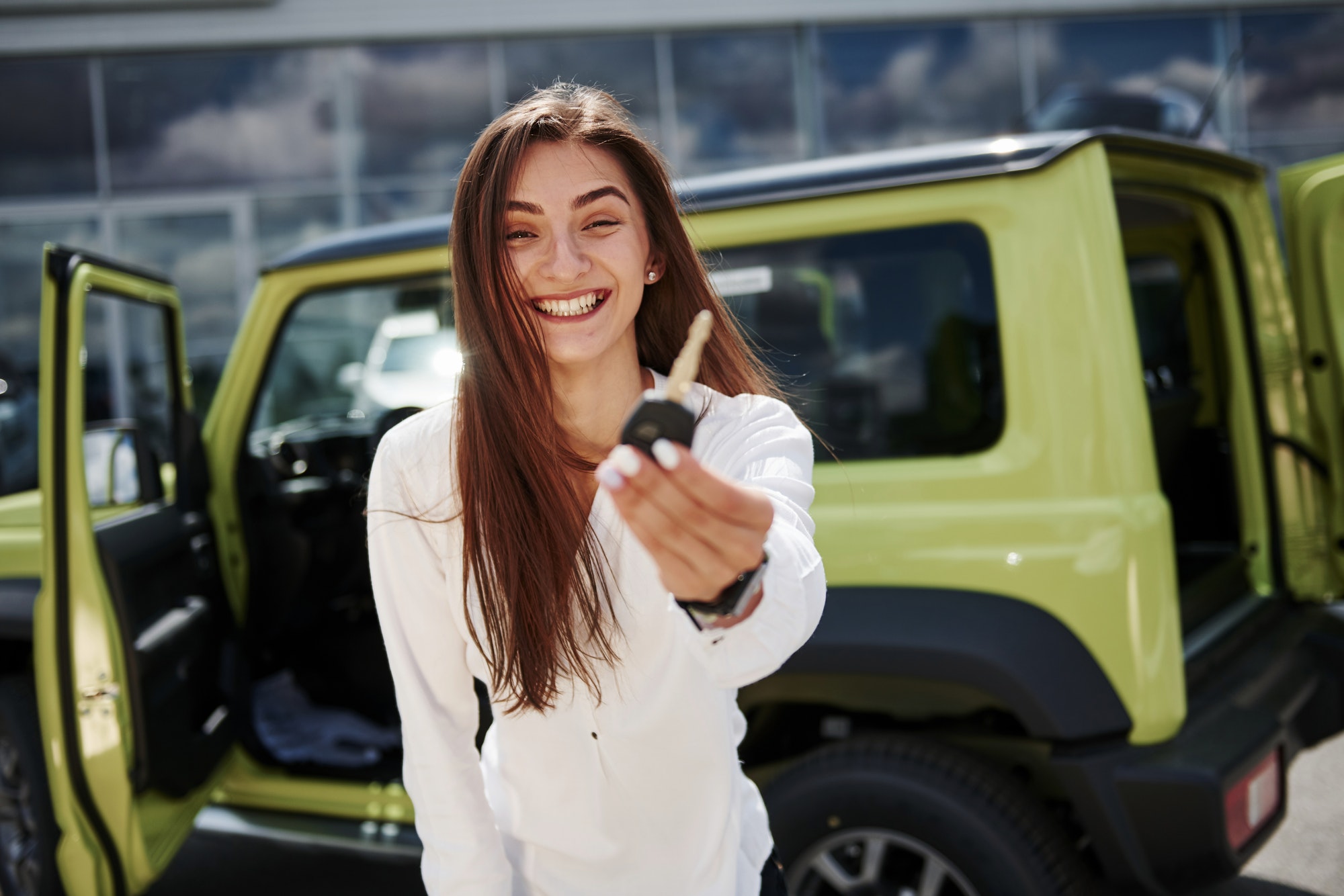 Young woman in white official clothes stands in front of green automobile outdoors Young woman in white official clothes stands in front of green automobile outdoors